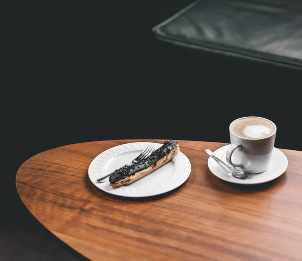 Φλιτζάνι καφέ στο ξύλινο τραπέζι με εκλαίρ — Φωτογραφία Αρχείου