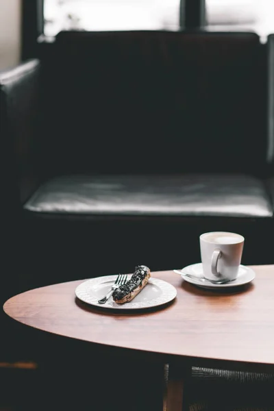 Šálek kávy na dřevěný stůl s Eclair — Stock fotografie