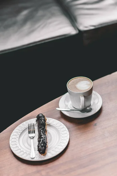 Kopp kaffe på träbord med éclair — Stockfoto