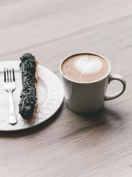 Taza de café sobre mesa de madera con eclair — Foto de Stock