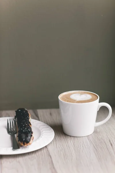 Taza de café sobre mesa de madera con eclair — Foto de Stock