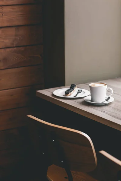 Xícara de café na mesa de madeira com eclair — Fotografia de Stock