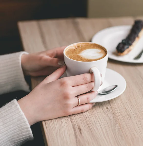 Frauenhände um eine Tasse auf Holztisch mit Schokolade gewickelt — Stockfoto