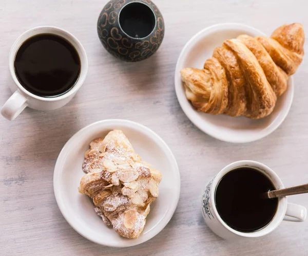 Сніданок на білому столі з чашками кави та круасанами — стокове фото