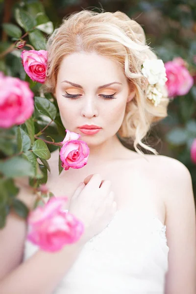 Piękna Brunetka Panna Młoda w pobliżu kwitnienia Bush róże pozowanie w sukni ślubnej — Zdjęcie stockowe