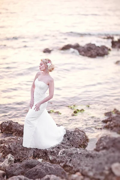 Jovem noiva morena de vestido branco Posando junto ao mar ao pôr do sol — Fotografia de Stock