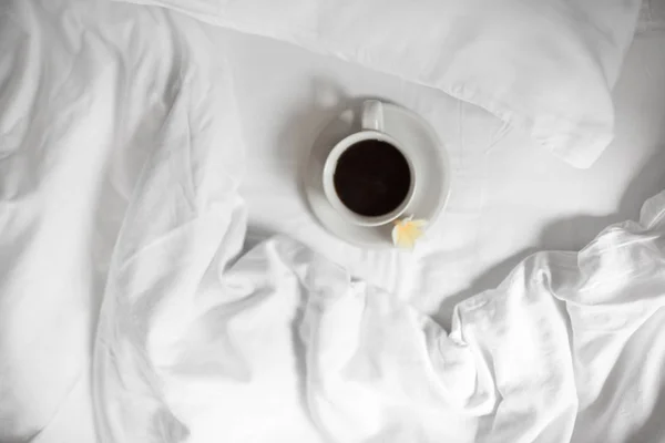 Une tasse de café noir est debout sur un lit blanc — Photo