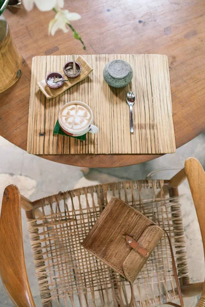 木製のテーブルにカプチーノのカップ。竹スタイル。籐のバッグ — ストック写真