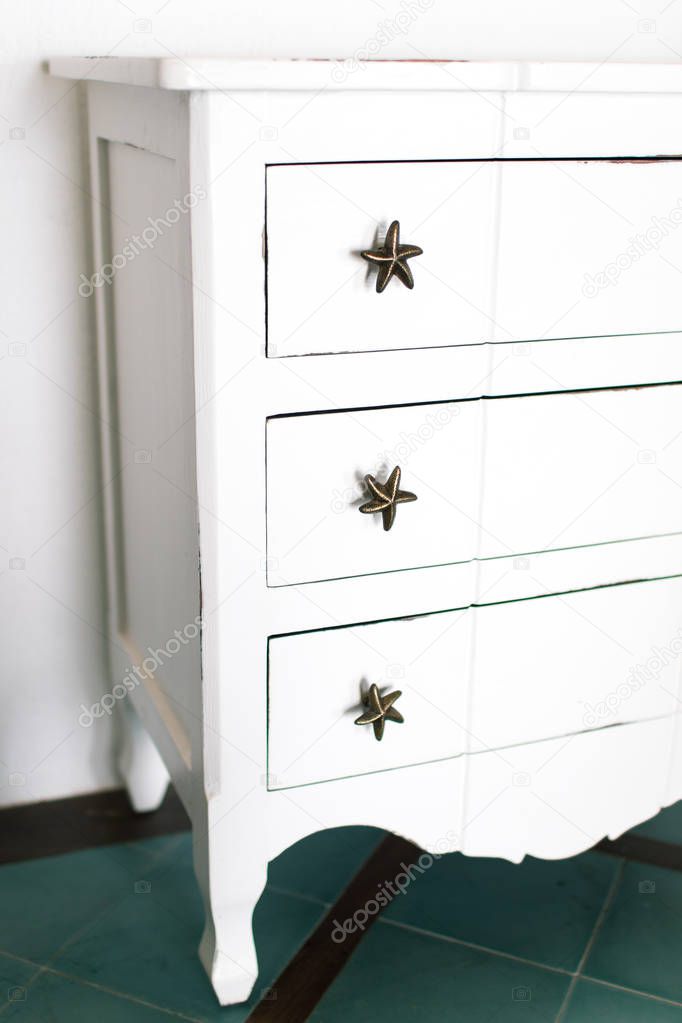 White vintage chest of drawers stands near white wall