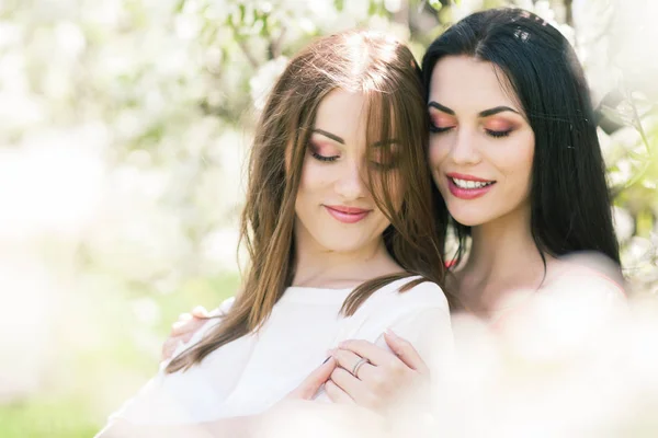 Two beautiful girls stand in a blossoming garden, play silly and — Stock Photo, Image