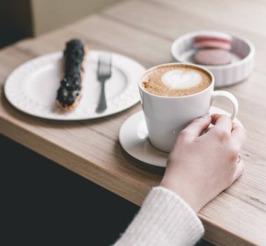 Bir fincan çikolatalı e ile ahşap masa üzerinde kadının elleri sarılı