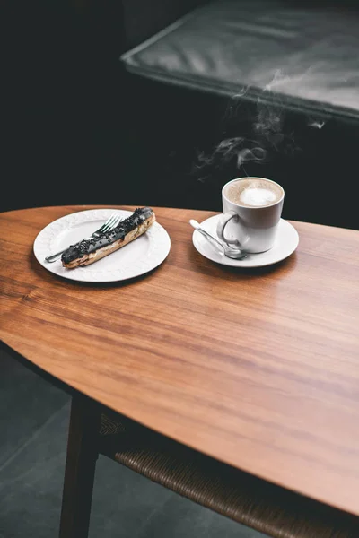 Xícara de café na mesa de madeira com eclair — Fotografia de Stock