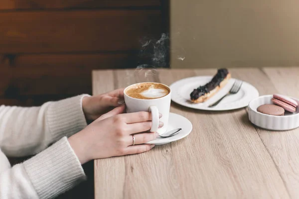 Bir fincan çikolatalı e ile ahşap masa üzerinde kadının elleri sarılı — Stok fotoğraf