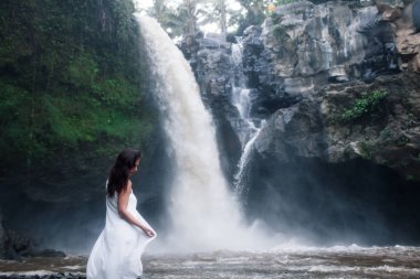 Young Girl in White Clothes Walking near a Waterfall Tegenungan  clipart