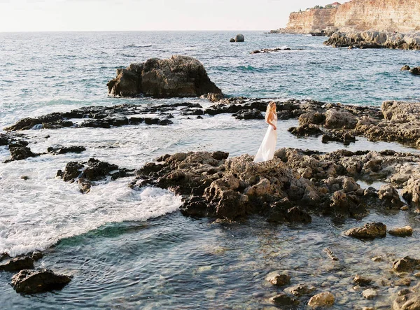 Ξανθιά Νύφη θέτοντας σε βράχια κοντά στην θάλασσα. Λεπτή και ειλικρινείς φωτογραφίες. Νυφικά στο εξωτερικό. Γάμος στην παραλία — Φωτογραφία Αρχείου