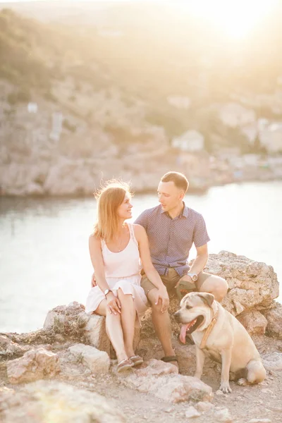 Casal de caras brincando com seu cão na montanha perto do oceano — Fotografia de Stock