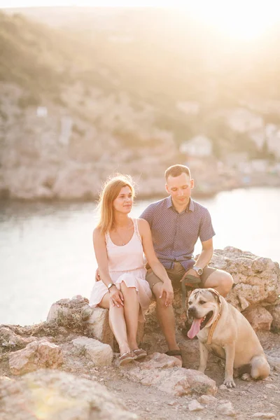 Casal de caras brincando com seu cão na montanha perto do oceano — Fotografia de Stock