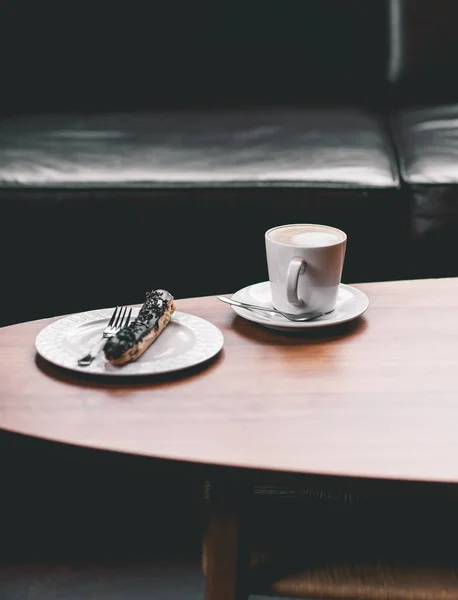 Xícara de café na mesa de madeira com eclair — Fotografia de Stock