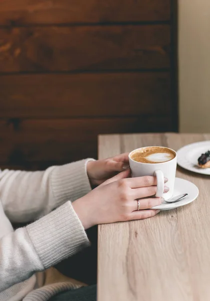 Bir fincan çikolatalı e ile ahşap masa üzerinde kadının elleri sarılı — Stok fotoğraf