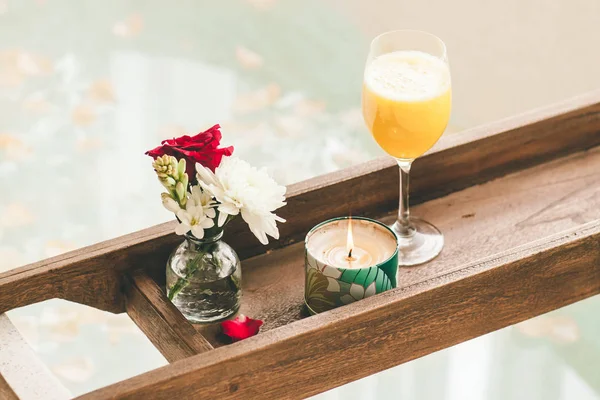 Bright Bathroom at Home. Bath with Flower Petals and Salt. Tray over the Bath with Orange Juice, Notepad and Candles.