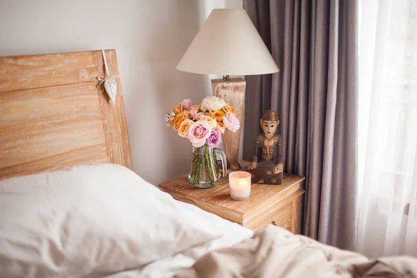 Деревянная кровать с белыми простынями. A Bedside Table by the bed with a — стоковое фото