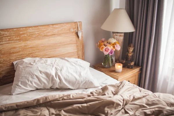 Cama de madeira com lençóis brancos. Uma mesa de cabeceira ao lado da cama com um — Fotografia de Stock