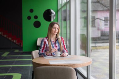 Kız bir kafede oturuyor ve bir fincan kahve tutuyor