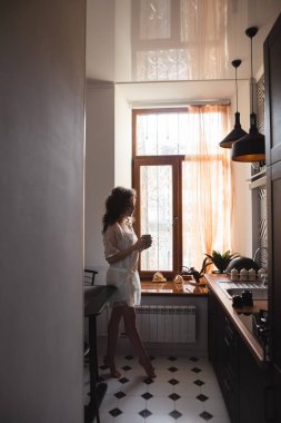 Kız bir fincan kahve cam kenarında ile mutfakta