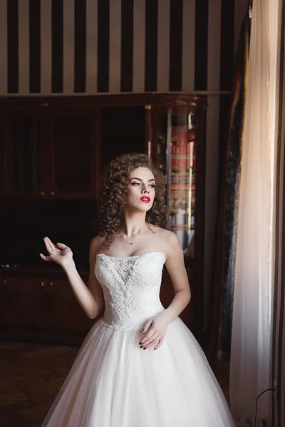 Chica elegante de pie junto a la ventana vestida con un vestido de novia —  Fotos de Stock