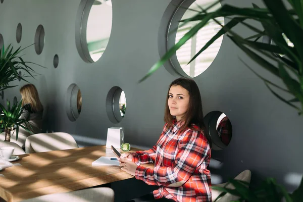 Estudiante sentada en un café en las manos de su teléfono móvil —  Fotos de Stock