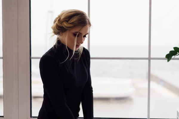 A beautiful girl with her head down, standing by the window of a cafe — Stock Photo, Image