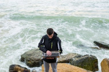 bir adam bir kayada duran ve bir dizüstü bilgisayar alkışlar