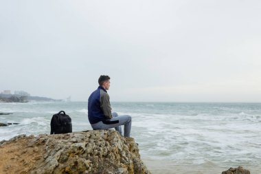 adam bir sırt çantası ile bir kayaya deniz üzerine oturur.