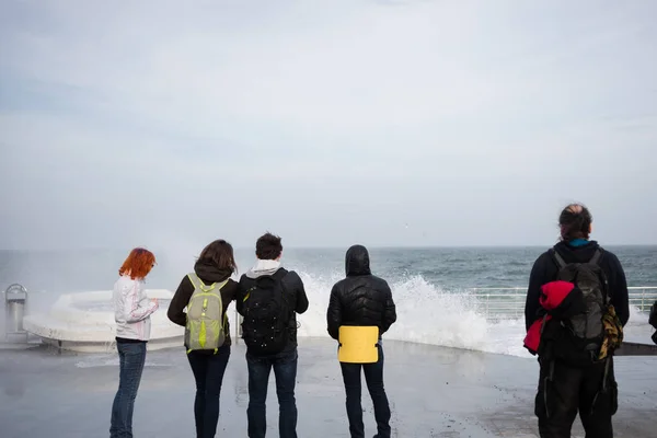 people stand on the beach by the sea during a storm and look at the waves