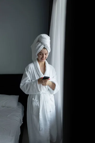 Женщина в халате стоит у окна и читает сообщение . — стоковое фото
