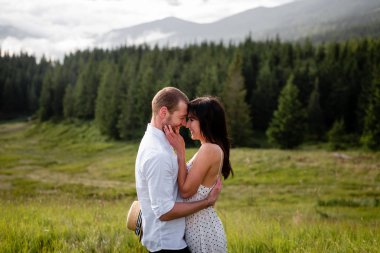 Erkek ve güzel esmer, sık bir ormanın arka planında birbirlerine bakarlar.