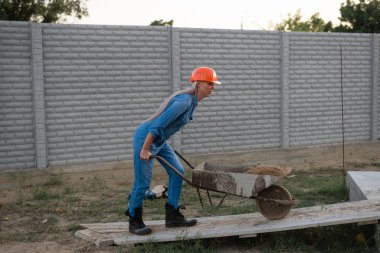 İnşaat alanında çalışan bir kadın, kum arabası taşıyor.