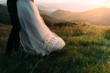 Gelin ve damat, belden aşağısı resmedilmiş bir şekilde tepede dururlar.