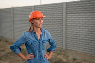 Turuncu kasklı bir kadın inşaat alanında duruyor.