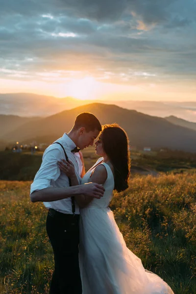 De bruid en bruidegom knuffelen elkaar, de bergen en de zonsondergang op de achtergrond — Stockfoto