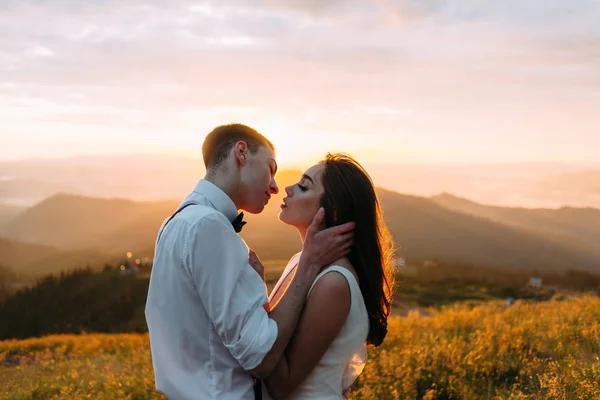 Ein Mann und eine Frau küssen sich im Hintergrund des Sonnenuntergangs, Frischvermählte in den Bergen — Stockfoto