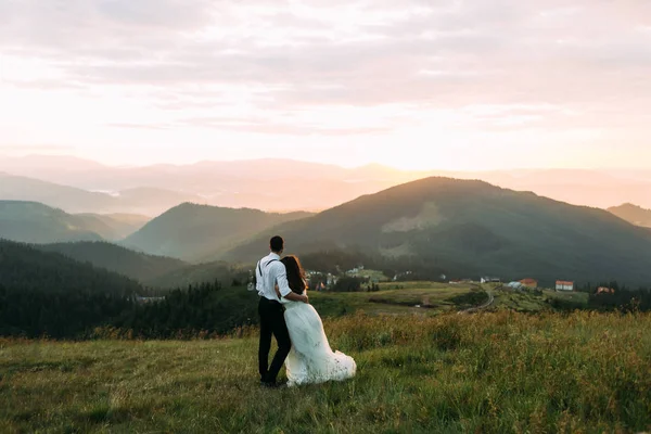 Recién casados disfrutan de la puesta de sol en las montañas, vista desde la parte posterior — Foto de Stock