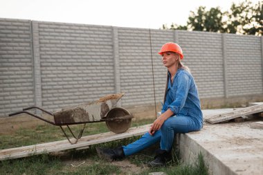 İnşaat üniformalı güzel bir kadın oturur ve önüne bakar.