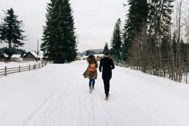 Sırt çantalı bir adam ve bir kız karda yolda yürüyorlar.