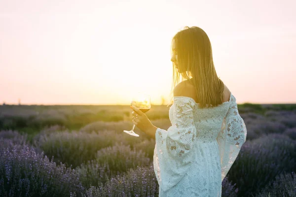 A woman with a glass of wine stands in the sun, lavender field — 图库照片