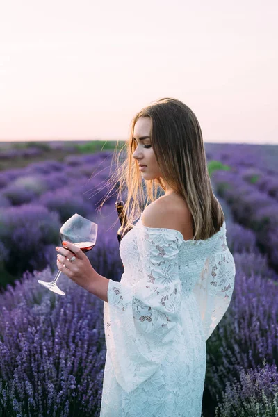 A woman holds a bottle of wine and a glass of lavender in the background — 图库照片
