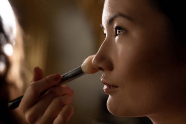 Makyaj sanatçısı, modelin yüzüne, stüdyonun içinde bir fırçanın yakın plan portresiyle pudra sürüyor..