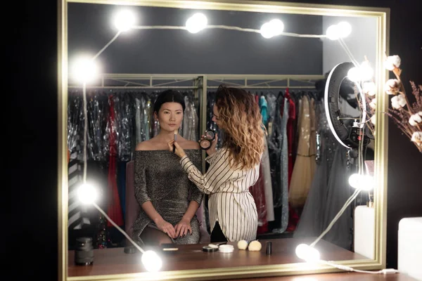 Makyaj sanatçısı güzellik salonunda güzel Asyalı kadın yapıyor, aynada yansıması var.