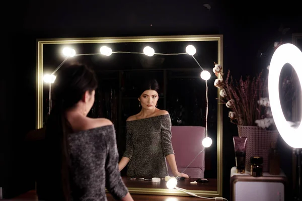 The girl stands in front of the mirror in flashlights and examines her makeup in the beauty salon