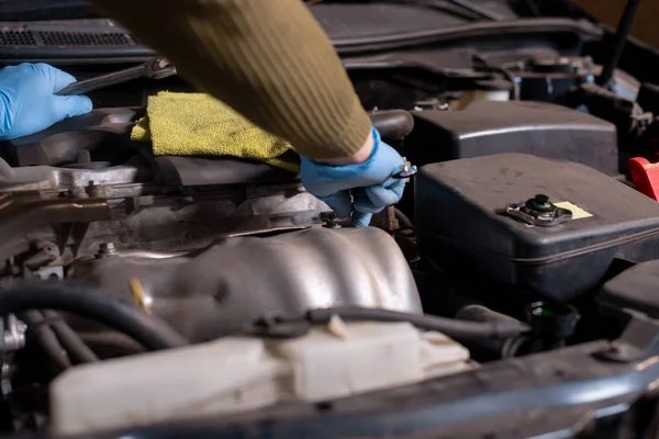 Mechanic unspins bolt under car bonnet holding wrenches in hand, close-up. Car repair